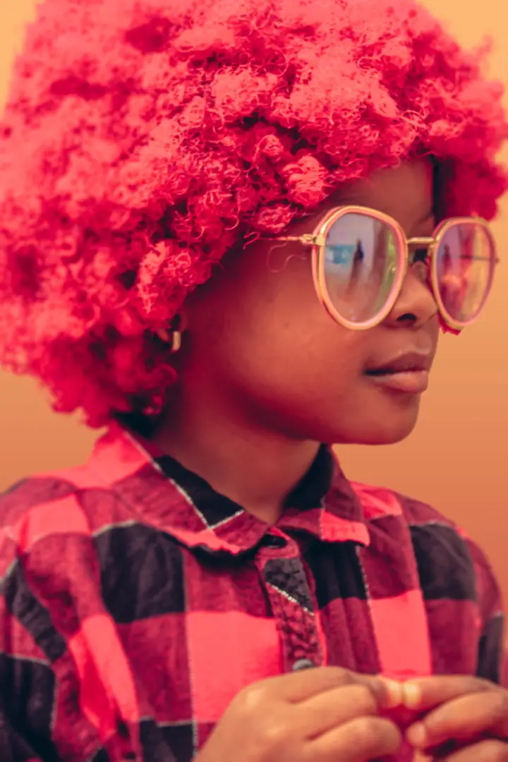 Child with a red afro wearing large clear glasses
